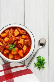 Potatoes stewed with meat, in tomato sauce, with spices and herbs, no people, on a white table
