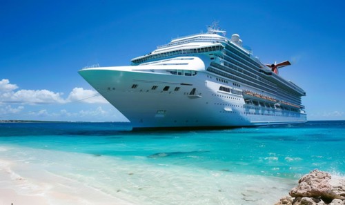 A large cruise ship is docked at the beach. The ship is white and is surrounded by a blue ocean.