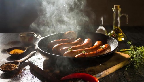 A frying pan of hot beef and pork sausages being grilled with spices and oil on a rustic table, AI