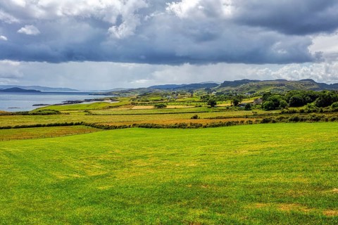 Extensive coastal landscape with sea, meadows and cloudy skies, near the Great Pollet Sea Arch