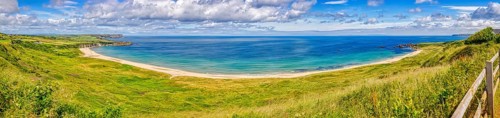 Wide beach with green meadow and wide sea under a blue, cloudy sky, County Antrim Coast