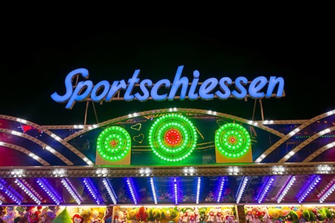 Illuminated sports shooting sign on a fairground stand with colourful lights at night, Cannstatter
