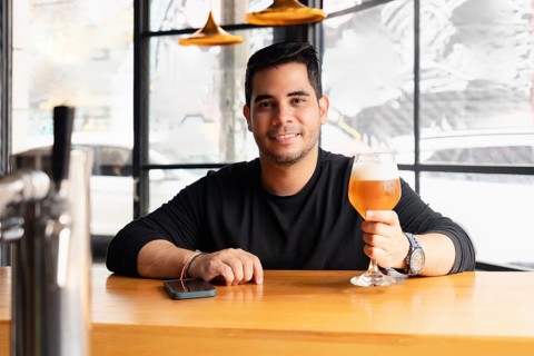A young Latin man enjoys a refreshing lager beer in a chic, modern bar. He is sitting at the