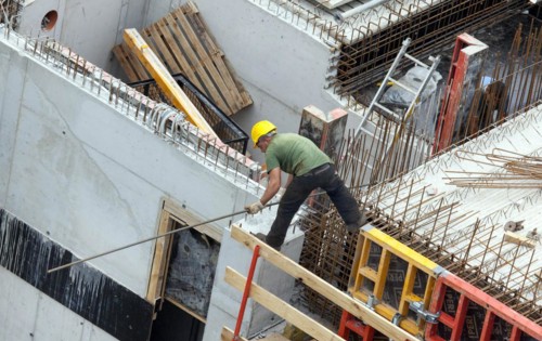 A construction worker juggles with an iron bar in his hand on a building site at lofty heights,