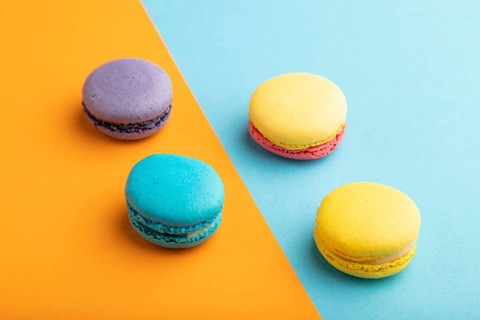 Yellow, purple and blue macaroons on blue and orange pastel background. side view, close up.
