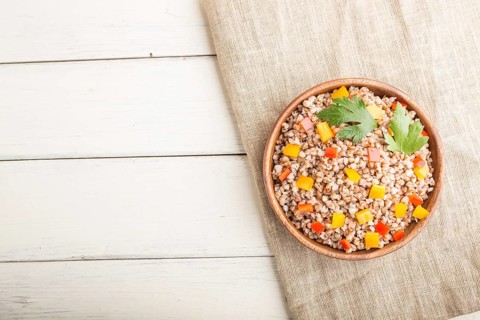 Buckwheat porridge with vegetables in wooden bowl on a white wooden background and linen textile.