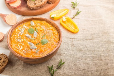 Sweet potato or batata cream soup with sesame seeds in a wooden bowl on a white wooden background