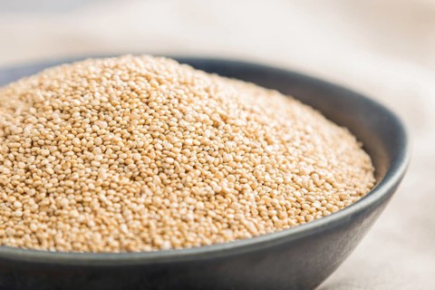 Blue ceramic bowl with raw white quinoa seeds on a gray concrete background and linen textile. Side