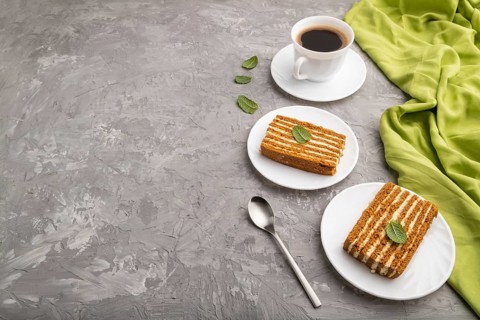 Homemade honey cake with milk cream and mint with cup of coffee on a gray concrete background and