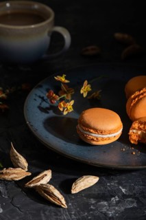 Orange macarons or macaroons cakes with cup of coffee on a black concrete background. Hard light,