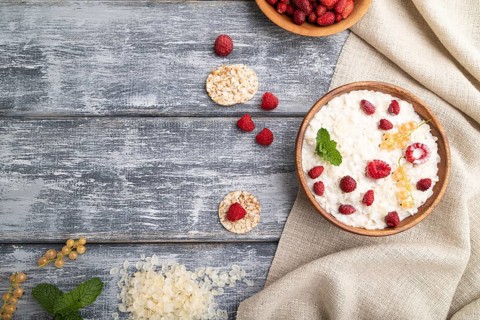 Rice flakes porridge with milk and strawberry in wooden bowl on gray wooden background and linen
