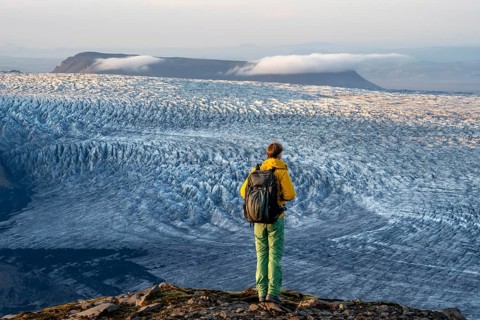 Young man, tourist in front of impressive glacier, in the evening light, glacier tongues