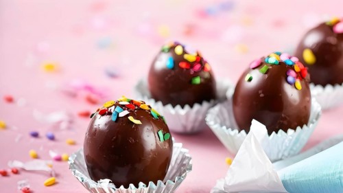 Small chocolate Easter eggs wrapped in shiny foil, placed on a bed of shredded pastel-colored