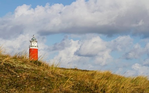 A red lighthouse stands on a grassy hill under a dramatic cloudy sky, Eierland lighthouse, Texel