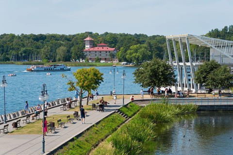 A lively lakeside promenade with a view of the lake, boats and an architectural bridge in the