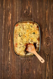 A casserole filled with cannelloni pasta, vegetables and herbs in a glass dish. A wooden spatula