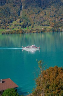 A ship cruises across the lake, against a background of forested mountains in autumn colours, Lake