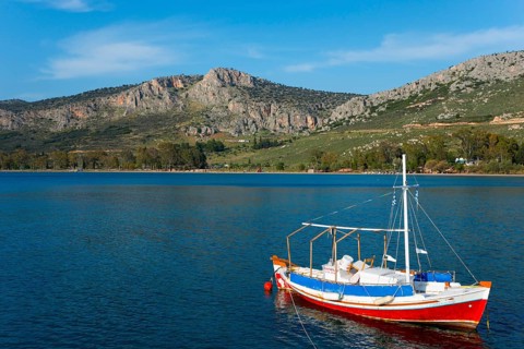 Small boat on a calm sea with mountains and blue sky in the background, Agia Kyriaki, Nafplio,