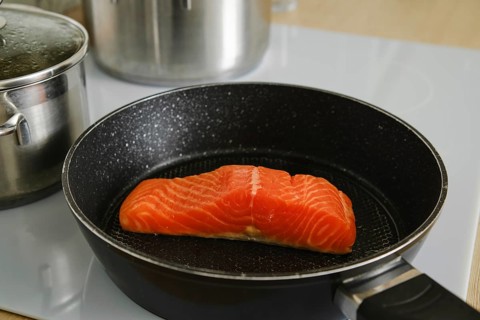 Closeup view of piece of fresh trout steak in a frying pan on electric stove