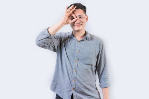 Happy young man making ok gesture with hand looking through fingers. Smiling person making ok
