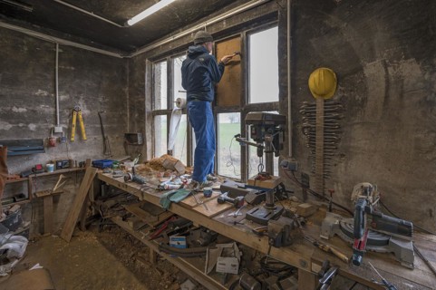 Young man in his workshop, standing on the workbench and repairing a window,