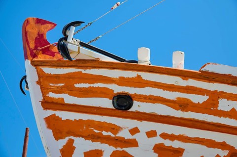 Close-up of the bow of a sailboat with orange and white paint and anchor in front of a blue sky,