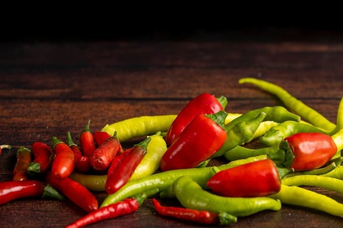 Green and red peppers scattered on a dark wooden surface, food photography