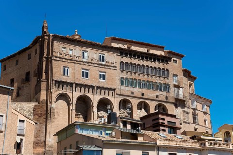 Large historic stone building with several windows and balconies under a clear blue sky, episcopal
