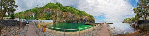 360° view, wooden walkway leading to green rocky coast and clear ocean under blue sky with clouds,