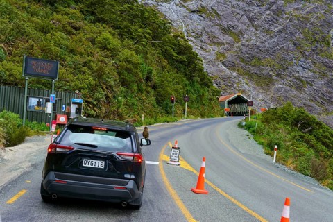 A car standing in front of a red light at a tunnel opening, surrounded by forest and mountains and