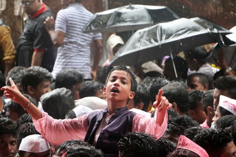 A boy braves the rain dances procession leading a gigantic idol of Hindu god Ganesh immersion