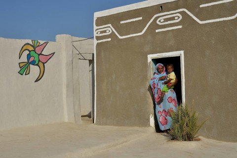 Woman carrying toddler, colorful painted Nubian house in the village Umogaal in Dongola, Nubia,