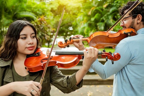 Violinist man and woman back to back playing violin in a park outdoors. Two young violinists