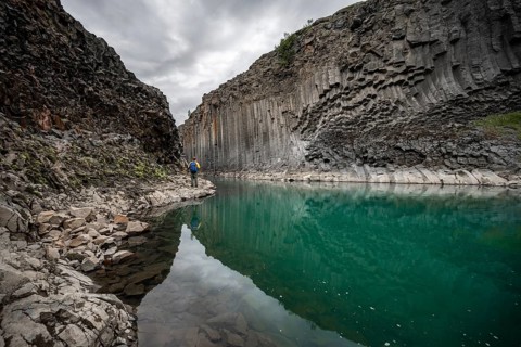 Tourist standing by the river in Stuðlagil Canyon, turquoise blue river between basalt columns,