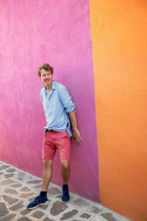 Young man leaning against a pink and orange house wall, colourful houses on the island of Burano,