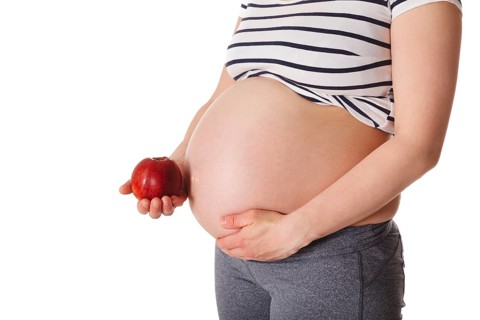 Healthy eating and diet during pregnancy concept, pregnant woman standing and holding red apple
