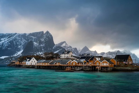 Traditional yellow rorbuer cabins on Sakrisøy Island, snow-capped rocky mountains in the back,