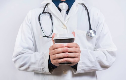 Hands of doctor holding takeaway coffee on isolated background. Doctor hands holding paper coffee