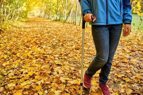 Young teenage girl walks with crutch through colourful autumn leaves