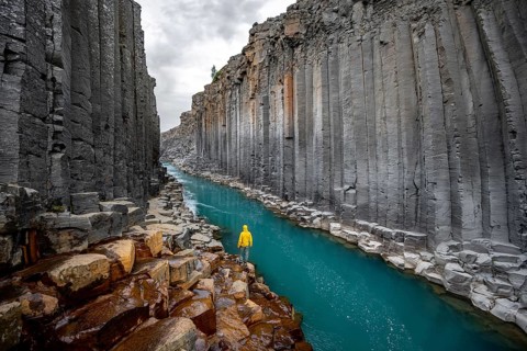 Tourist standing by the river in Stuðlagil Canyon, turquoise blue river between basalt columns,