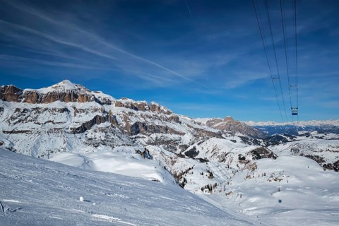View of a ski resort piste with people skiing in Dolomites in Italy with cable car ski lift. Ski