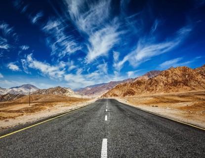 Travel forward concept background, road in mountains Himalayas with dramatic clouds on blue sky.