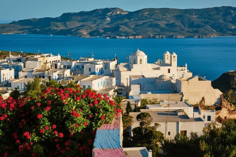 Picturesque scenic view of Greek town Plaka on Milos island over red geranium flowers. Plaka