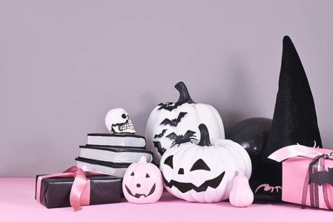 Pink and white Halloween decor with black and white pumpkins, witch hat and spell books on gray