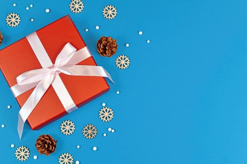 Red Christmas gift box with ribbon surrounded by seasonal pine cones and wooden snowflake ornaments