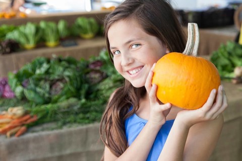 Happy young blue eyed girl holding a fresh pumpkin at the farmers market