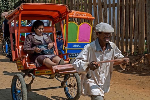 Old Malagasy man pulling pousse-pousse, pulled rickshaw with local woman in the city Antsirabe,