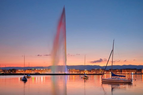 The Jet d'eau at dusk is the landmark in Geneva's harbour basin, with sailboats in the foreground