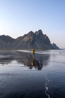 Tourist at black lava beach, sandy beach and sea, mountains Klifatindur reflected in the water,