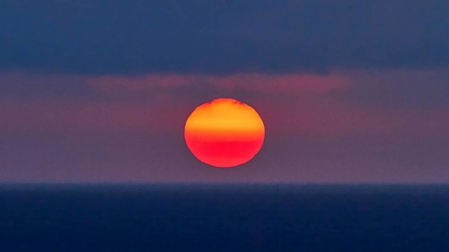 Sun as a fiery red big ball, blue-purple sky, sun just above the horizon, sunset, evening light,